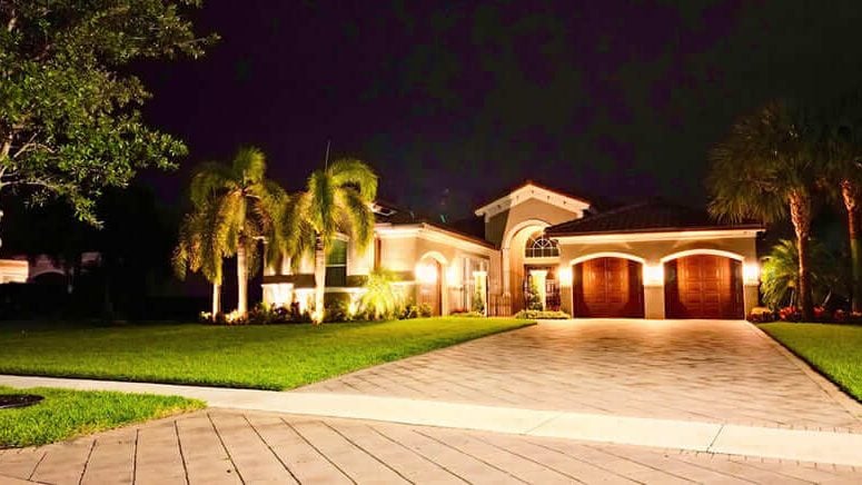 Warm low-voltage landscape lighting washing the facade and uplighting palms at a Fort Lauderdale home at night