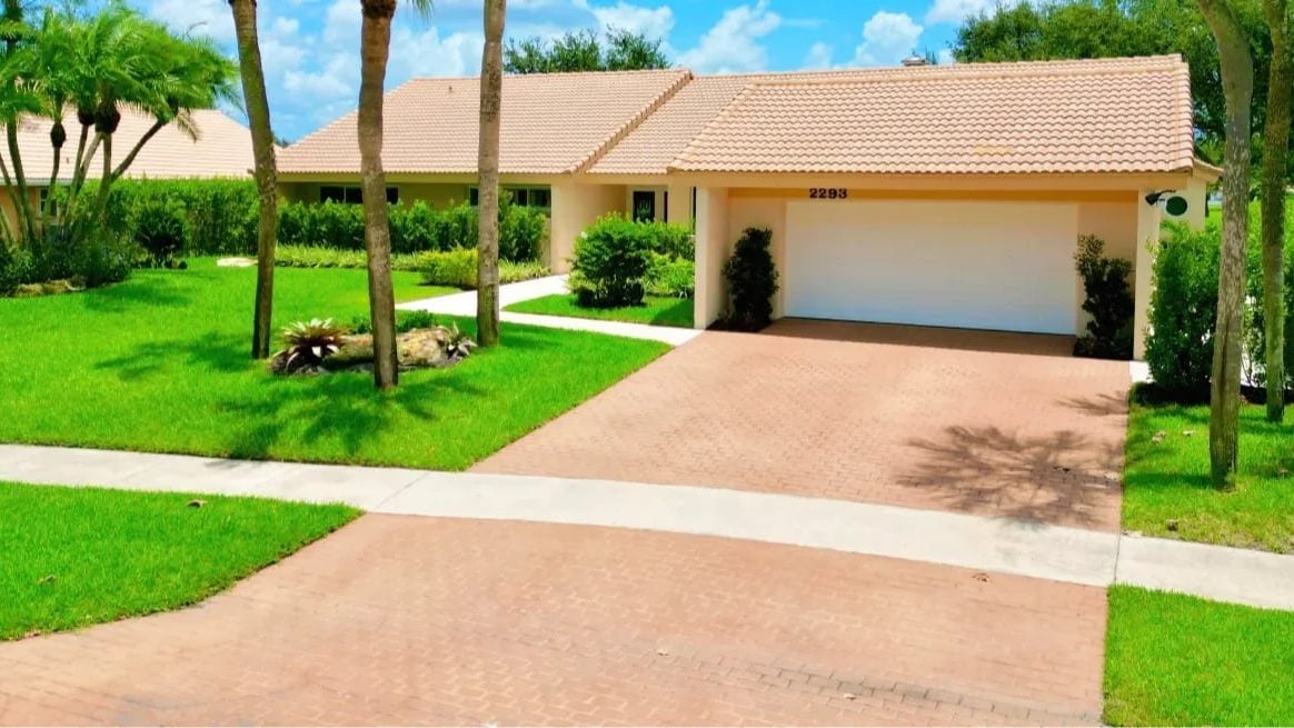 Paver driveway and poured concrete walkway at a single-story South Florida home with palms and a tile roof